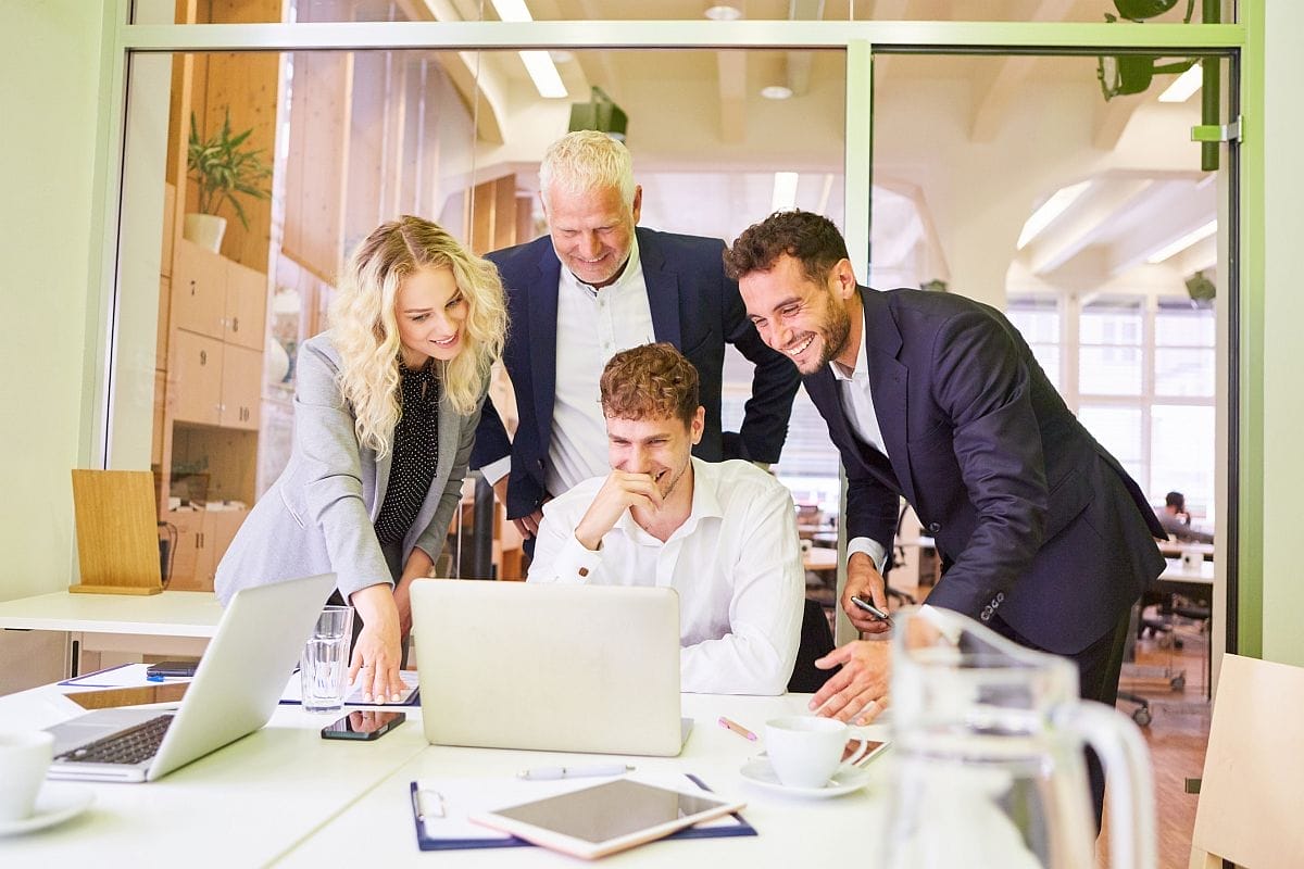 Professional business people grouped around a laptop, looking happy; successful product launch concept