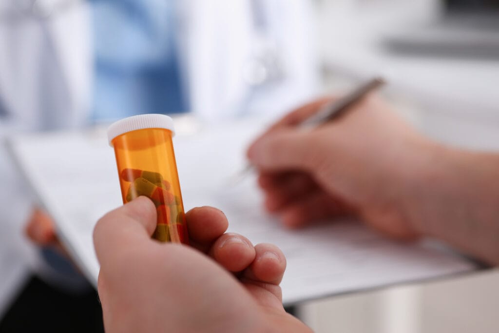 Close-up of hand holding a pill bottle and writing prescription